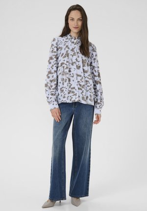 Long-sleeve blouse with a light blue and brown abstract print, featuring pleats and button closure. Paired with wide-leg denim and beige shoes.