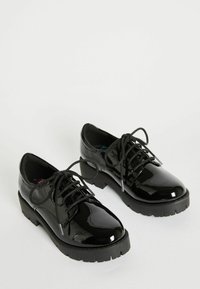 Scarpe stringate in vernice nera con suola spessa, dotate di punte arrotondate e una finitura liscia e lucida. Lacci neri e suola testurizzata.