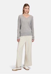 Světle šedý svetr s výstřihem do V z měkkého pleteného materiálu, kombinovaný s krémovými kalhotami s širokými nohavicemi a bílými teniskami. Jednoduchý, moderní design a volný střih.