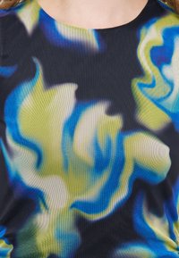 Κοντινή λήψη υφάσματος με κυματιστό αφηρημένο μοτίβο σε μπλε, πράσινες, λευκές και μαύρες αποχρώσεις σε ένδυμα που φορά ένα άτομο.