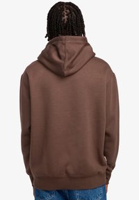 Braunfarbener Hoodie mit geräumiger Kapuze, aus weichem Material und mit gerippten Bündchen. Die Rückseite ist schlicht und weist keine zusätzlichen Designs oder Verzierungen auf.