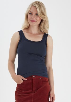 Marineblauwe tanktop met een ronde halslijn, slim fit en zachte stof, gecombineerd met een rode corduroy rok.
