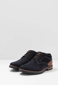 Chaussures lacées en daim bleu foncé avec des accents en cuir marron, bout arrondi, couture contrastante et semelle en caoutchouc.