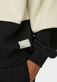 Schwarz und cremefarbene, farblich abgesetzte Sweatshirt mit geripptem Saum und Bündchen. Enthält ein Etikett im schwarzen Bereich. Weicher, strukturierter Stoff.