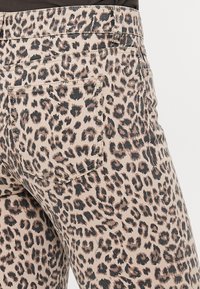 Džínsy s leopardím vzorem na béžovém podkladu, s tmavými skvrnami, středním pasem a standardními zadními kapsami. Texturovaný, přiléhavý design.