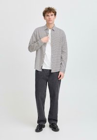 Camisa de botones con un patrón geométrico en blanco y negro, usada sobre una camiseta blanca, combinada con pantalones anchos oscuros y zapatos negros.