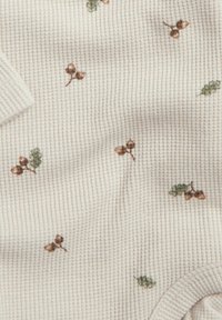 Tissu en coton avec un motif texturé en relief de couleur blanc cassé, présentant des motifs éparpillés de glands bruns et de feuilles vertes.