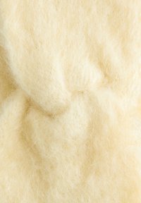 Natürlicher Wollstoff in weicher, flauschiger Textur. Helles Cremetier mit dezenten Fasern und unterschiedlicher Dicke. Keine auffälligen Muster oder Akzente.