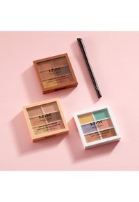 Trois palettes de correcteurs NYX dans des étuis orange, beige et blanc, chacune comportant quatre sections avec différentes teintes, accompagnées d'un pinceau noir.