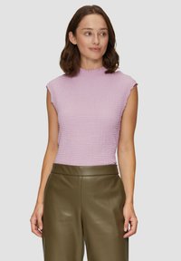 Korte mouw lilac top met een gestructureerd patroon en een gekartelde halslijn, gecombineerd met hoge groene leren broeken.