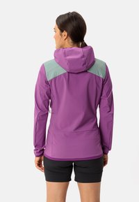 Lila Outdoor-Jacke mit hellgrünen Schulterakzenten, Kapuze und figurbetontem Design. Hergestellt aus flexiblem, strukturiertem Stoff. Schwarze Shorts sind darunter sichtbar.