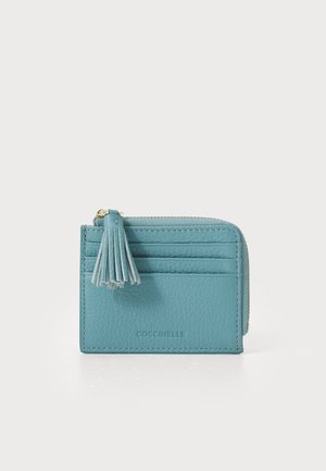 Portafoglio in pelle verde acqua con finitura testurizzata, diversi slot per carte, chiusura con zip e un nappo decorativo attaccato alla cerniera.