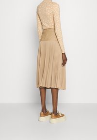 Beige långärmad topp med blommönster, tillsammans med en veckad beige kjol och bruna platåskor, som visar upp mjuka texturer och lagerdesign.