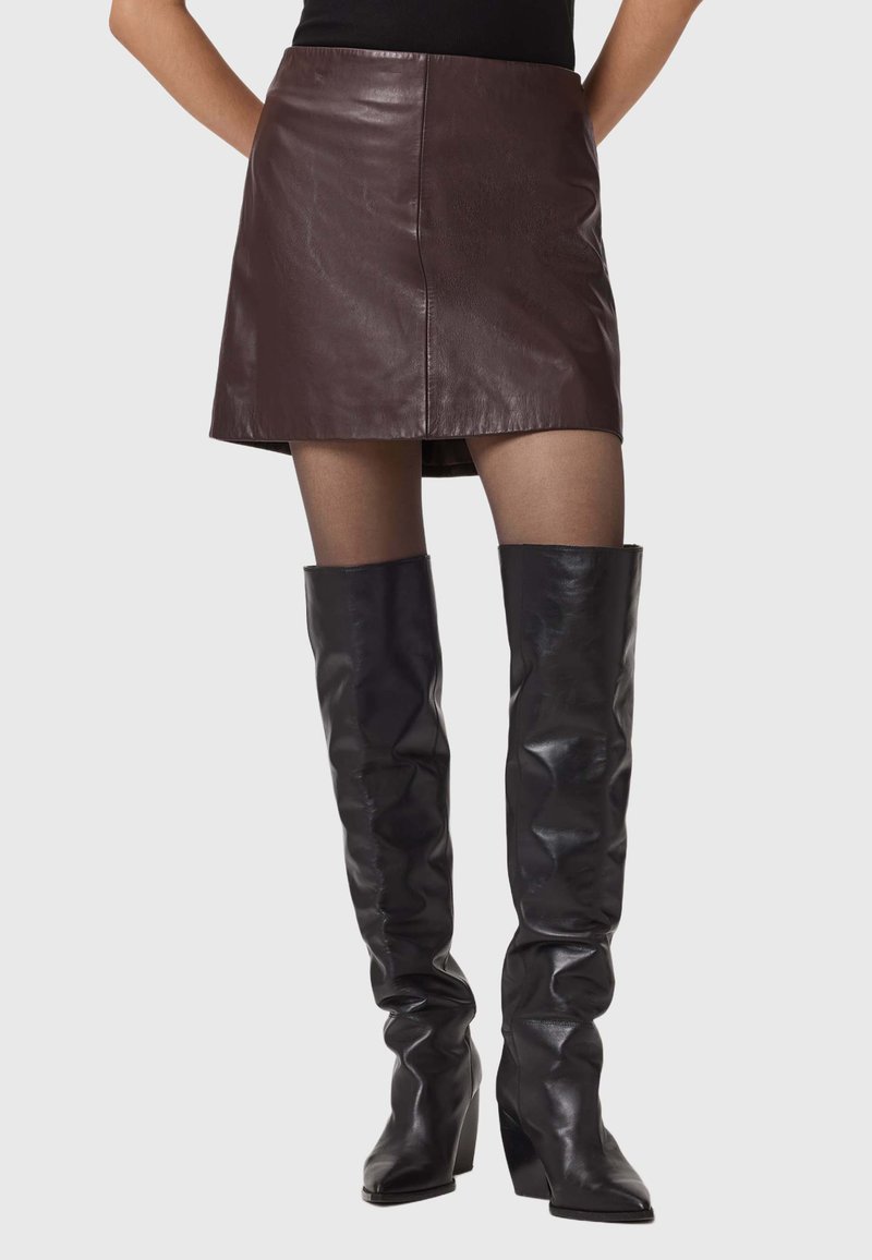 Mini-jupe en cuir bordeaux assortie à des bottes noires au-dessus du genoux avec un large talon. Texture lisse avec un minimum de détails.