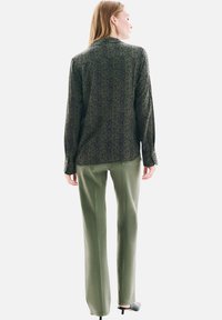 Chemise à rayures vertes à manches longues, associée à un pantalon vert olive. L'ensemble présente une coupe décontractée et une texture subtile.