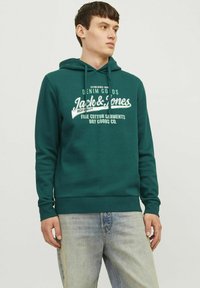 Grøn bomulds hoodie med et frontgrafiktryk, justerbar snoretræk, ribbede ærmer og kant. Sammen med lyseblå denimjeans.
