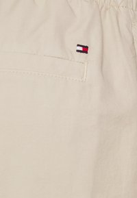 Beżowa tkanina o miękkiej fakturze ma haftowane logo w kolorze czerwonym, białym i niebieskim na kieszeni. Prosty fason z elastycznym pasem.