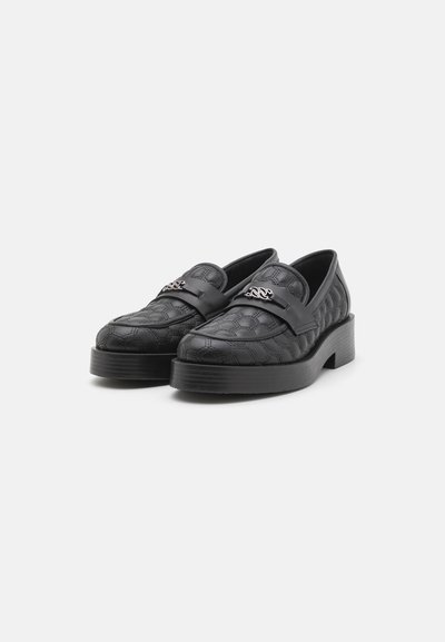 Melni loafers ar teksturētu, iešūtu rakstu, masīvu platformu un spīdīgu metālisku akcentu augšējā joslā.