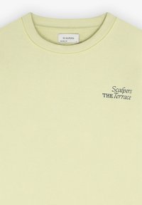 Sweatshirt léger jaune clair avec col rond côtelé, fabriqué en tissu doux. Présente un texte brodé "Scalpers THE Terrace" en vert foncé.
