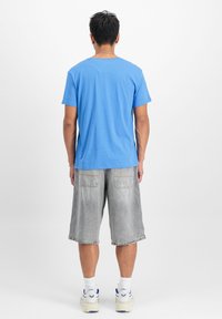 Zila kokvilnas T-krekls ar apaļu kakla izgriezumu, kombinēts ar pelēkiem džinsu šortiem. Redzama šūšana uz kabatām un apakšmalas. Vienkāršs, ikdienišķs dizains.