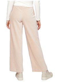 Pantalon large en velours côtelé beige clair, avec une texture côtelée verticale et une taille élastique. Associé à des baskets beiges.