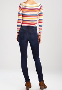 Randig långärmad topp i flera färger med vid halsringning, tillsammans med mörkblå tajta jeans med bakfickor och en slät finish.