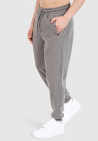 Grijze sweatpants met een elastische tailleband, zijzakken en een subtiele merklabel. Gecombineerd met witte sneakers. Zachte stof textuur.