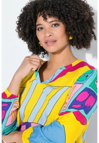 Blusa colorida que presenta una mezcla de amarillo y azul con patrones geométricos audaces. Diseño de cuello en V con mangas elásticas. Textura de tela suave.