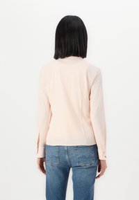 Soe roosa pikkade varrukatega särk, ümmarguse kaelusega ja nööpidega mansettidega, koos siniste teksastega. Sile tekstuur ja sobiv disain.