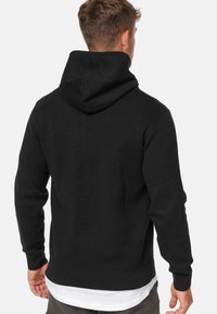 Zwarte hoodie met een trekkoord in de capuchon, geribde manchetten en zoom. Zachte textuur met een minimalistisch ontwerp, gedragen over een wit shirt.