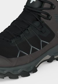 Chaussure de randonnée noire et grise avec semelle robuste, bout renforcé, lacets croisés et motif géométrique sur la partie supérieure.