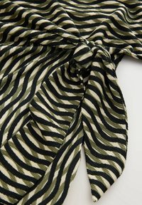 Tissu rayé zèbre noir, blanc et vert olive, torsadé en un nœud sur une surface claire.