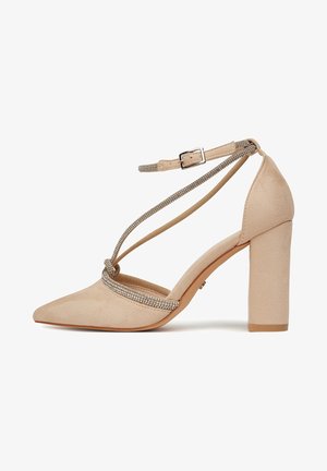 Zapato de tacón alto beige con punta afilada, material de ante, correa en el tobillo y banda decorativa de brillantes en la parte frontal.