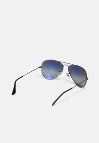 Ochelari de soare aviator din metal cu lentile graduată de culoare albastră, rame subțiri de culoare neagră și brațe negre. Dispun de suporturi pentru nas transparente pentru confort.