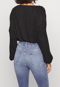 Svart långärmad topp med samlad baksida, matchad med ljusblå högmidjade jeans med bakfickor och en subtil tvättgradient.