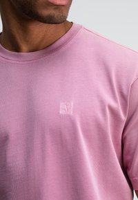 Lichtroze t-shirt met korte mouwen, gemaakt van zacht materiaal, met een kleine, reliëf logo op de borst en een ronde hals.