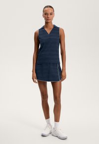 Mornarsko modra brezrokavnica z V-izrezom in teksturiranimi črtami, v kompletu z ujemajočo se krilom z belimi obrobami. Oblikovana z belimi športnimi čevlji.