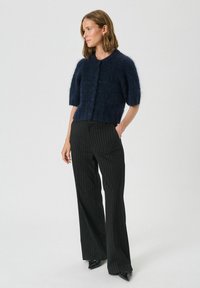 Cardigan scurt cu mâneci scurte, de culoare bleumarin, cu tricotaj texturat, guler rotund și cinci închideri cu nasturi, asortat cu pantaloni negri cu dungi fine.
