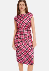 Enganliegendes Kleid im lebhaften pink-schwarzen Hahnentrittmuster, mit hohem Ausschnitt, kurzen Ärmeln und einem seitlichen Schlitz für zusätzliche Details.