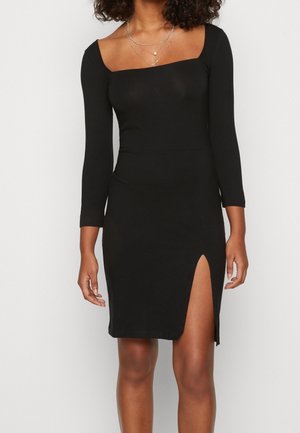 Musta bodycon-mekko pitkillä hihoilla, neliönmuotoinen pääntie ja sivuhalkio. Valmistettu joustavasta materiaalista tiukan ilmeen saavuttamiseksi.