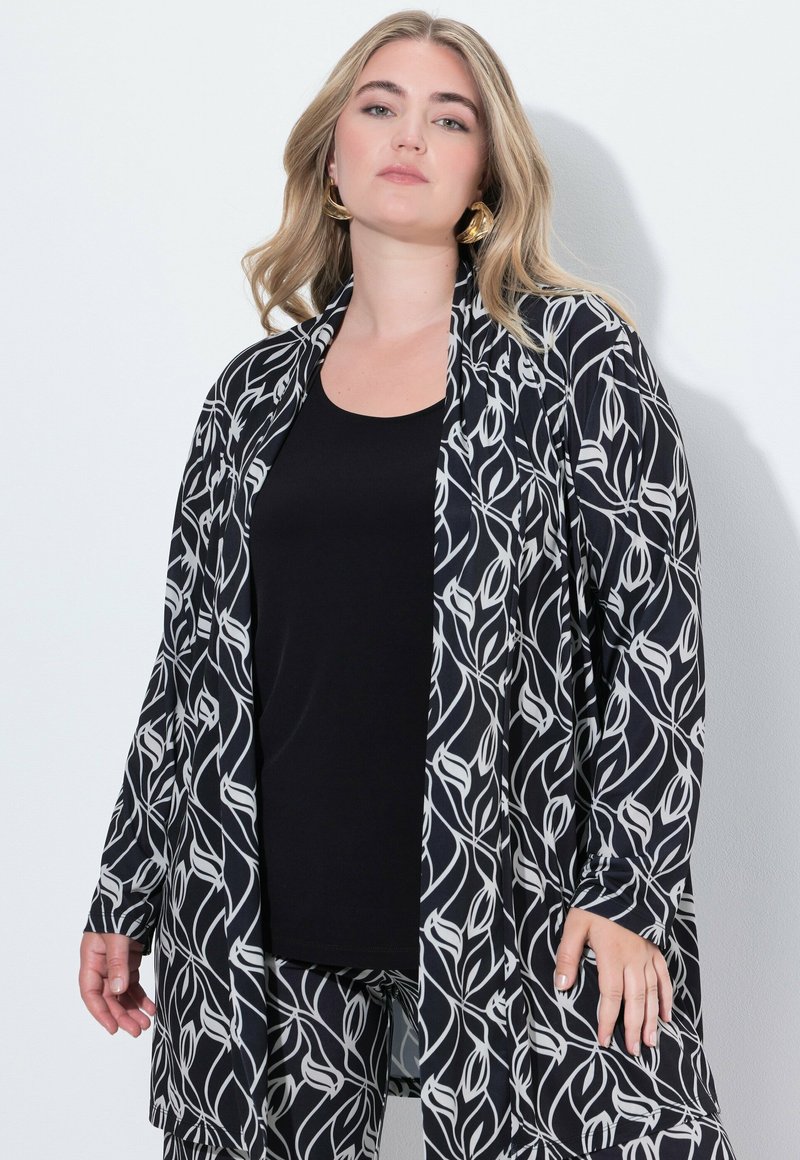 Černobílý kimono s květinovým vzorem, nošené přes černý tílko, s dlouhými rukávy a otevřeným předním dielom.