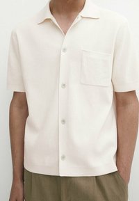 Korte mouwen, licht beige shirt van textuurstof, met een open kraag, knopen aan de voorkant en een enkele borstzak.
