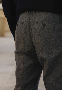 Gray herringbone trousers with a subtle pattern, two back pockets, and brown button accents, showcasing a tailored fit and textured fabric.