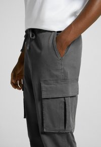 Grå cargo-byxor med dragsko i midjan, sidofickor och stora lårfickor, som har en slät yta och praktiska designfunktioner.