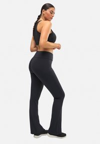 Sostenedor deportivo negro y mallas acampanadas hechas de un tejido elástico y suave. Las mallas cuentan con una cintura alta y una silueta ajustada.