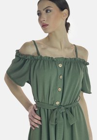 Vestido verde sin hombros con escote con volantes, cierres de botones de madera, mangas cortas y cintura con cinturón para una silueta fruncida.