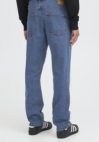 Plave traperice ravnog kroja s dva stražnja džepa i teksturiranim završetkom. Uparen s crnim cipelama koje imaju bijele pruge.