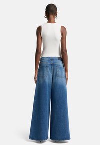 Breda denimjeans i medelblå tvätt med hög midja, bakfickor och en lätt blekning mot fållen. Slät textur.