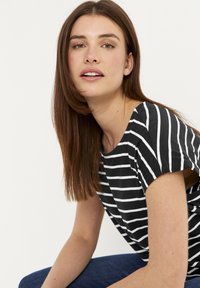 Sort og hvid stribet kortærmet top med rund udskæring. Har en afslappet pasform og blødt stof. Modellen poserer let drejet.