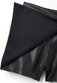 Pantaloni corti in pelle nera con una finitura morbida e spazzolata. La texture contrasta con la superficie liscia e lucida della pelle sottostante.